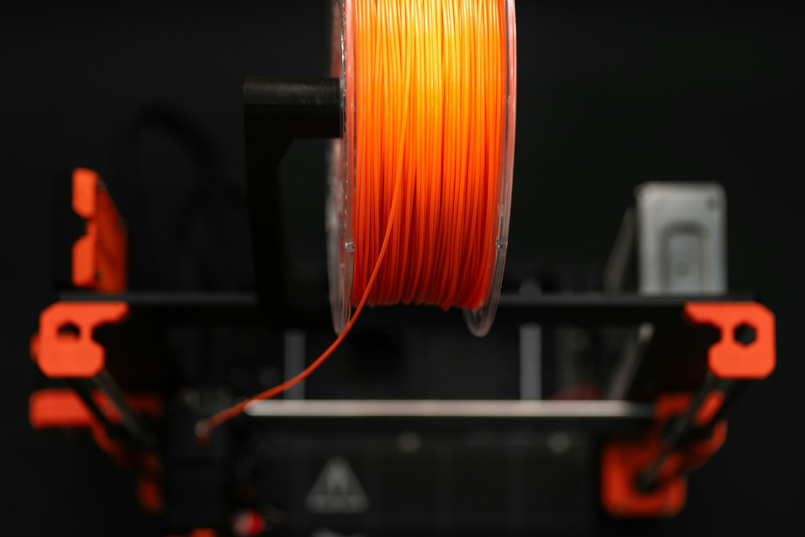 Spool of orange 3D-printer filament on a machine